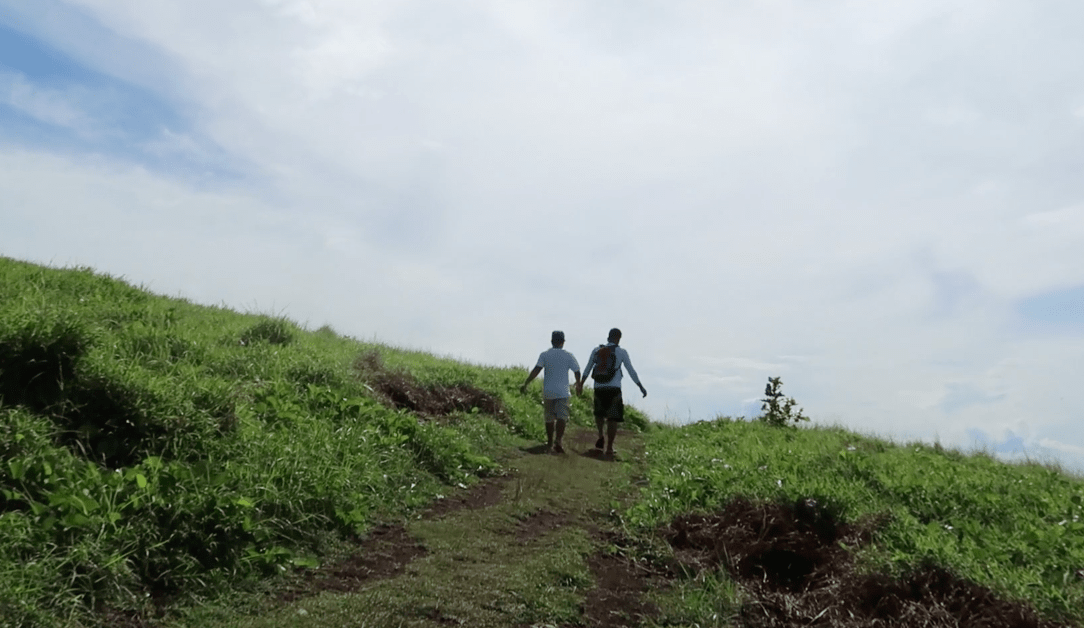 two filipino boys holding hands on a trail on a grassland in the philippines. Point Binurong natural landmark and landscape.
